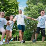 Group of joyful children playing outdoors with an instructor in a sunny park.